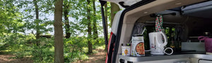 In der Kategorie Outdoor & Unterwegs präsentiert Lotao vegane und bio Fertiggerichte für unterwegs, hier im Kategoriebanner Desktop mit einer Camping-Küche im geöffneten Kofferraum vor Waldkulisse – ideale schnelle Fertiggerichte, Instant Gerichte und Fertiggerichte für den Wasserkocher.