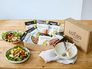 In der Kategorie Genussboxen präsentiert Lotao eine Auswahl an veganen Fertiggerichten in der Genussbox, hier im Kategoriebanner Mobil teils zubereitet auf Holztisch arrangiert.
