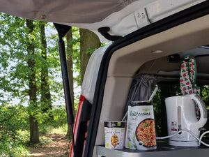 In der Kategorie Outdoor & Unterwegs präsentiert Lotao vegane und bio Fertiggerichte für unterwegs, hier im Kategoriebanner Mobil mit einer Camping-Küche im geöffneten Kofferraum vor Waldkulisse – ideale schnelle Fertiggerichte, Instant Gerichte und Fertiggerichte für den Wasserkocher.