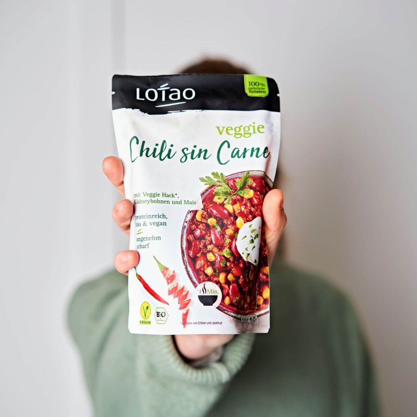 Hand hält 320g Packung der Lotao Veggie Chili sin Carne Bowl, einem bio-veganen Fertiggericht mit Lotao Veggie Hack, Kidneybohnen und Mais als vegane Bio-Mahlzeit