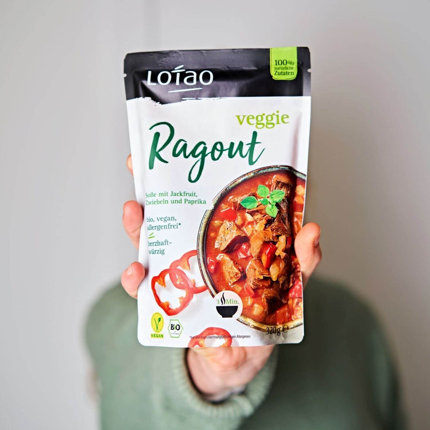 Hand hält 320g Packung Fertigsauce Veggie Ragout von Lotao mit bio-veganer Fertigsosse mit Jackfruit als veganer Fleischersatz, Zwiebeln und Paprika.