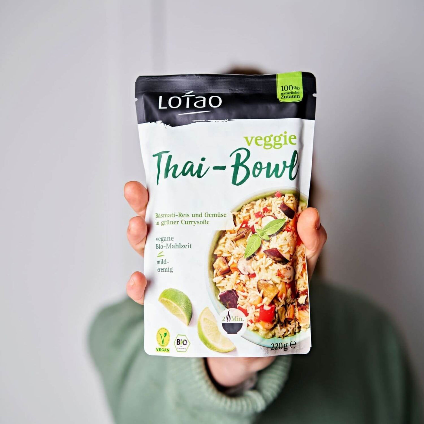 Hand hält 220g Packung der Lotao Veggie Thai Bowl, einem bio-veganen Fertiggericht mit Basmatireis und Gemüse in grüner Currysauce als vegane Bio-Mahlzeit