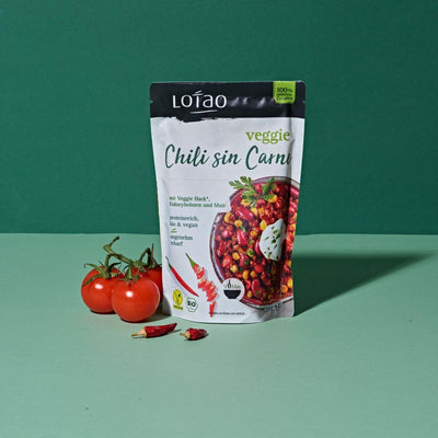 Grüner Hintergrund mit 220g Packung der Lotao Veggie Chili sin Carne Bowl, einem bio-veganen Fertiggericht mit Lotao Veggie Hack, Kidneybohnen und Mais als vegane Bio-Mahlzeit