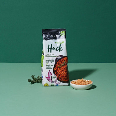 75g Packung vom Lotao Veggie Hack, dem veganen Fleischersatz auf Basis von Jackfruit und Erbsen in Bio-Qualität und mit einem Proteingehalt von über 70% und einem Schälchen vom Veggie Granulat vor grünem Hintergrund