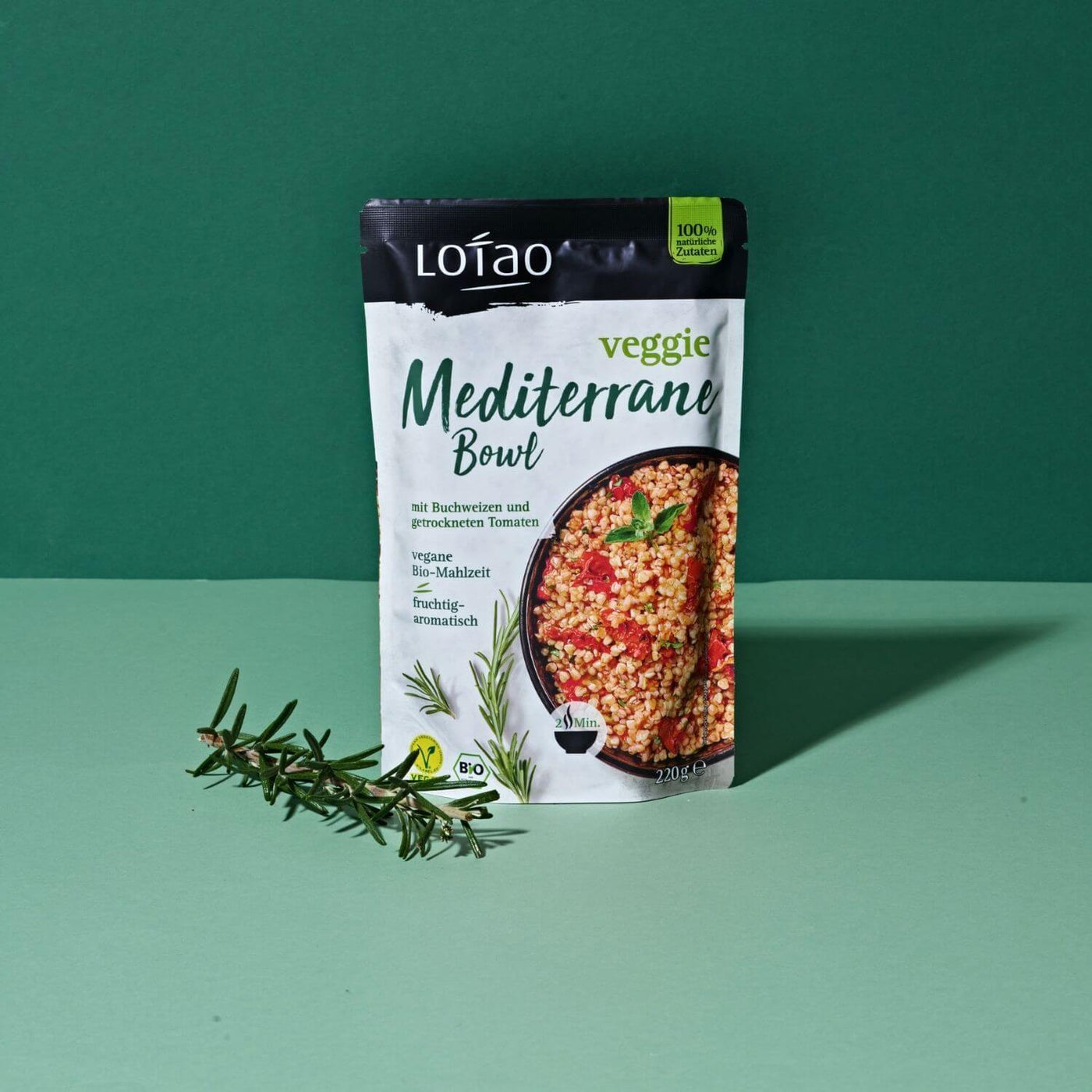 Grüner Hintergrund mit 220g Packung der Lotao Veggie Mediterranen Bowl, einem bio-veganen Fertiggericht mit Buchweizen und getrockneten als vegane Bio-Mahlzeit