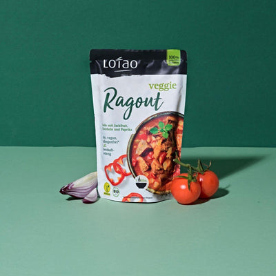 320g Packung Fertigsauce Veggie Ragout von Lotao mit bio-veganer Fertigsosse mit Jackfruit als veganer Fleischersatz, Zwiebeln und Paprika vor grünem Hintergrund