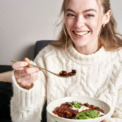 Frau genießt ihr Lotao Veggie Chili sin Carne Bowl, das bio-vegane Fertiggericht für ein schnelles Mittagessen oder ein gemütliches Abendessen